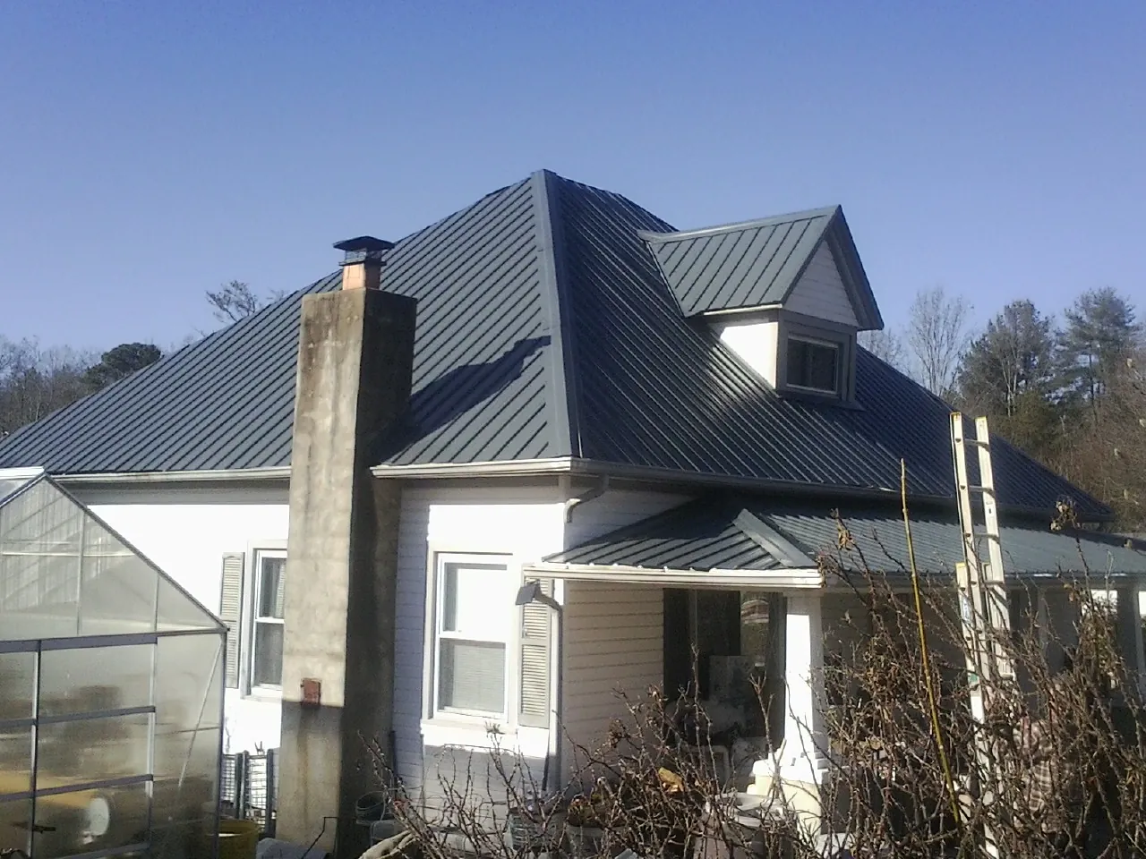 Dark blue standing seam metal roof on a white farmhouse with dormer — Slate & Tile Roof Repair by Roofing Brothers in Manor
