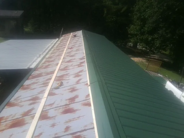 Old rusted panels beside newly installed green metal roofing — Wind Damage Roof Repair by Roofing Brothers in Manor