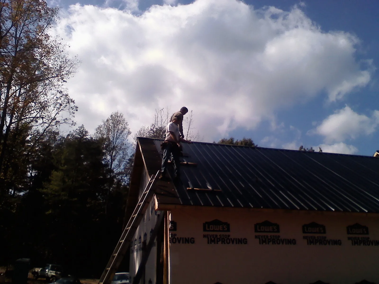 Roofer fastening dark metal panels high against a cloudy sky, from a Roof Inspection job in Manor