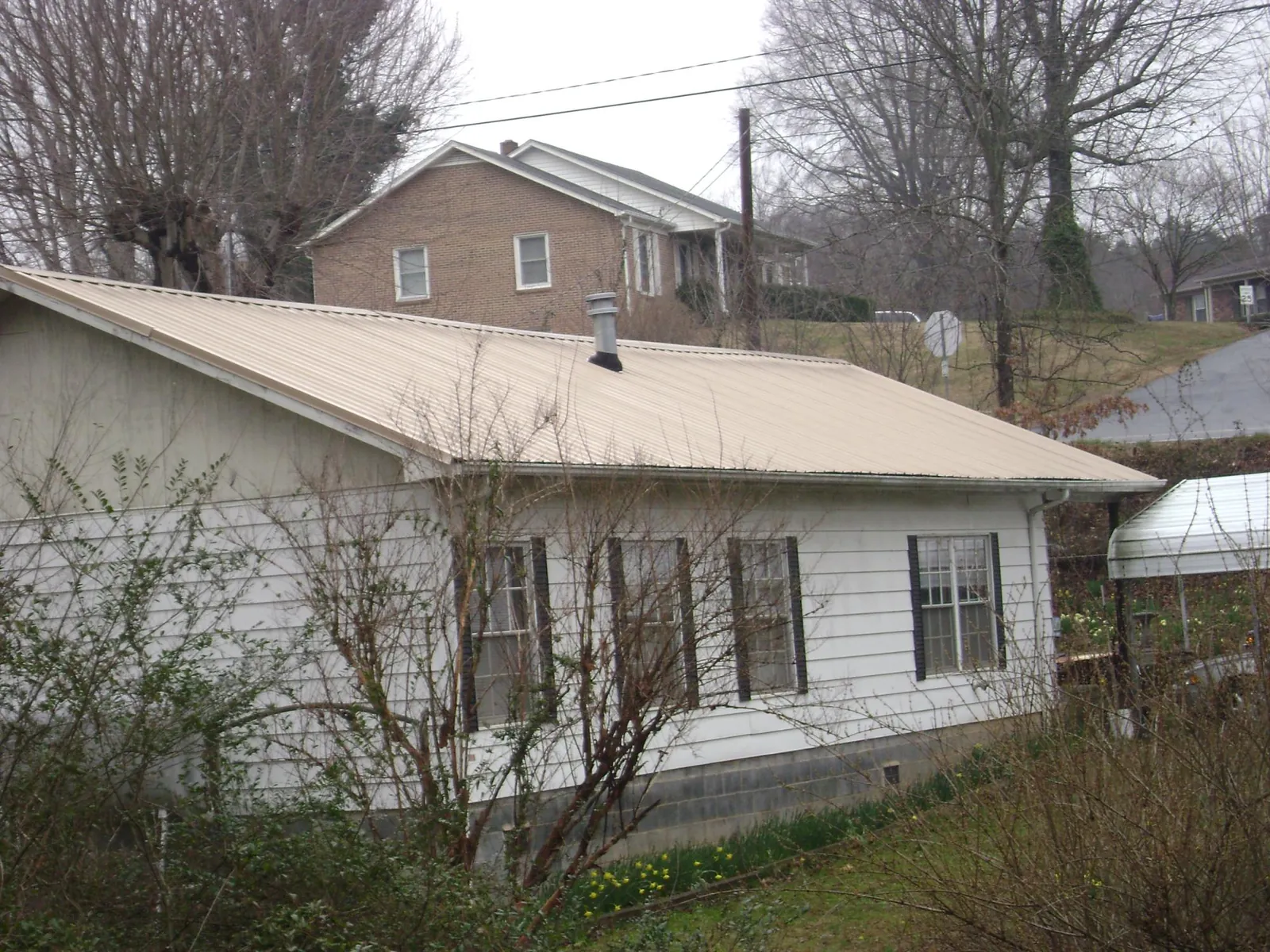 Tan metal roof on a white sided house set into a hillside — Commercial Roofing by Roofing Brothers in Manor