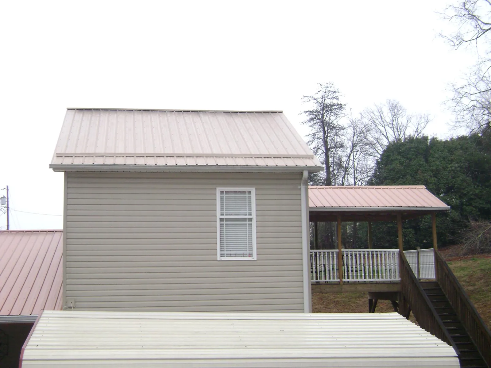 Tan metal roofs on a two story addition and attached porch, from a Roof Replacement job in Manor